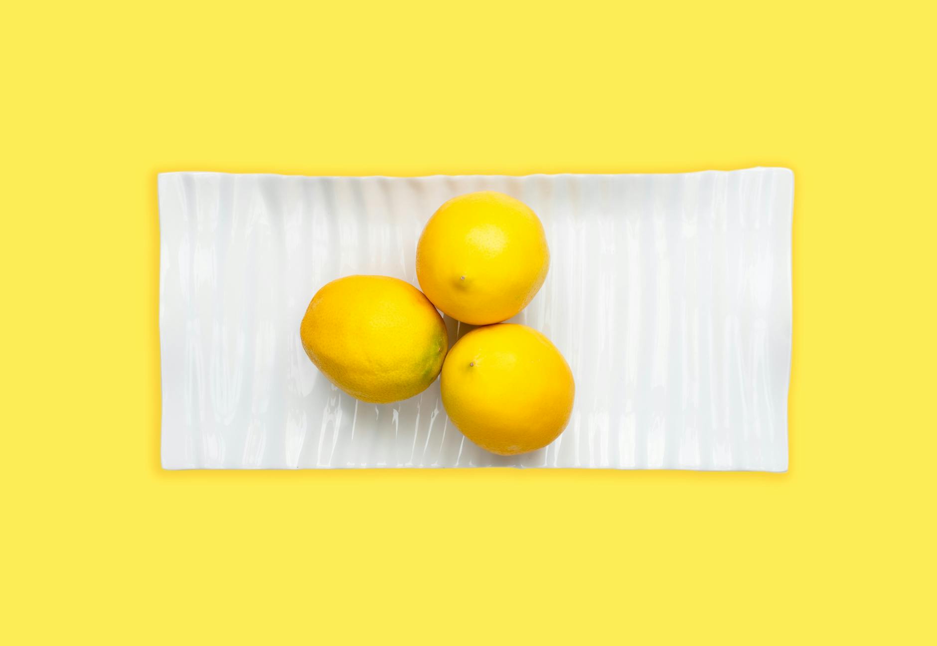 Fresh lemons arranged on a white plate with vibrant yellow background, symbolizing renewed pleasure and fresh starts