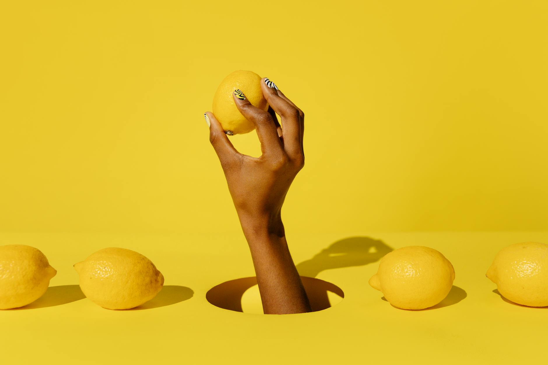Hand holding a lemon against a bright yellow background, symbolizing the fresh approach of lemon vibrators