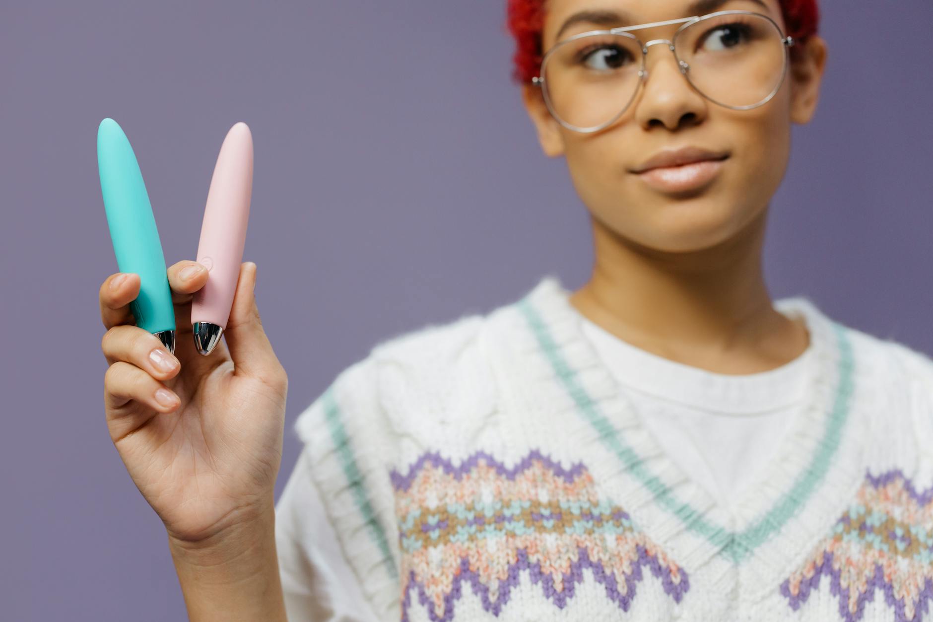 Woman holding colorful vibrators against a purple background, representing options for sexual pleasure at any age