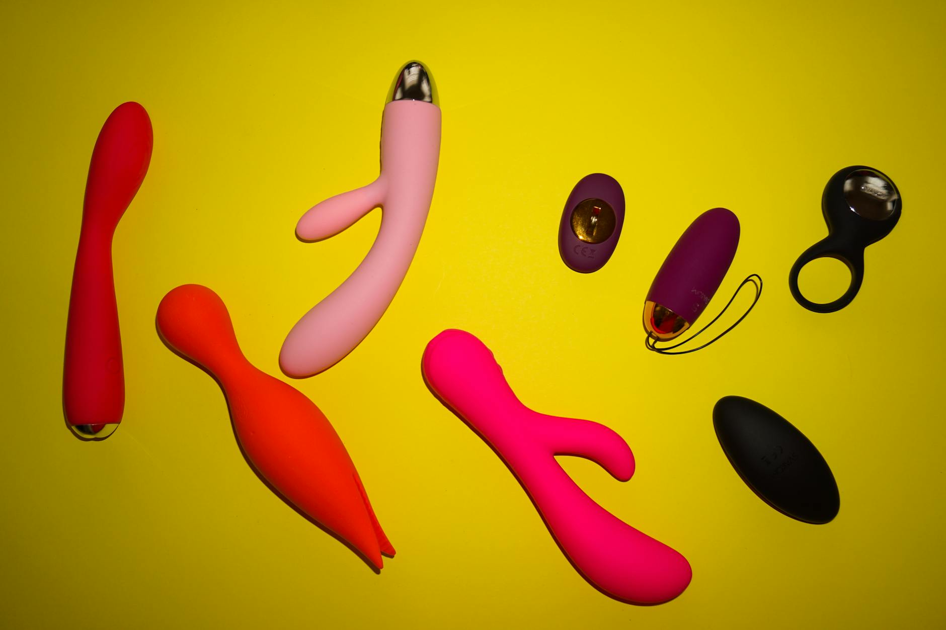 Colorful vibrators arranged on a bright yellow surface, representing diverse options for pleasure