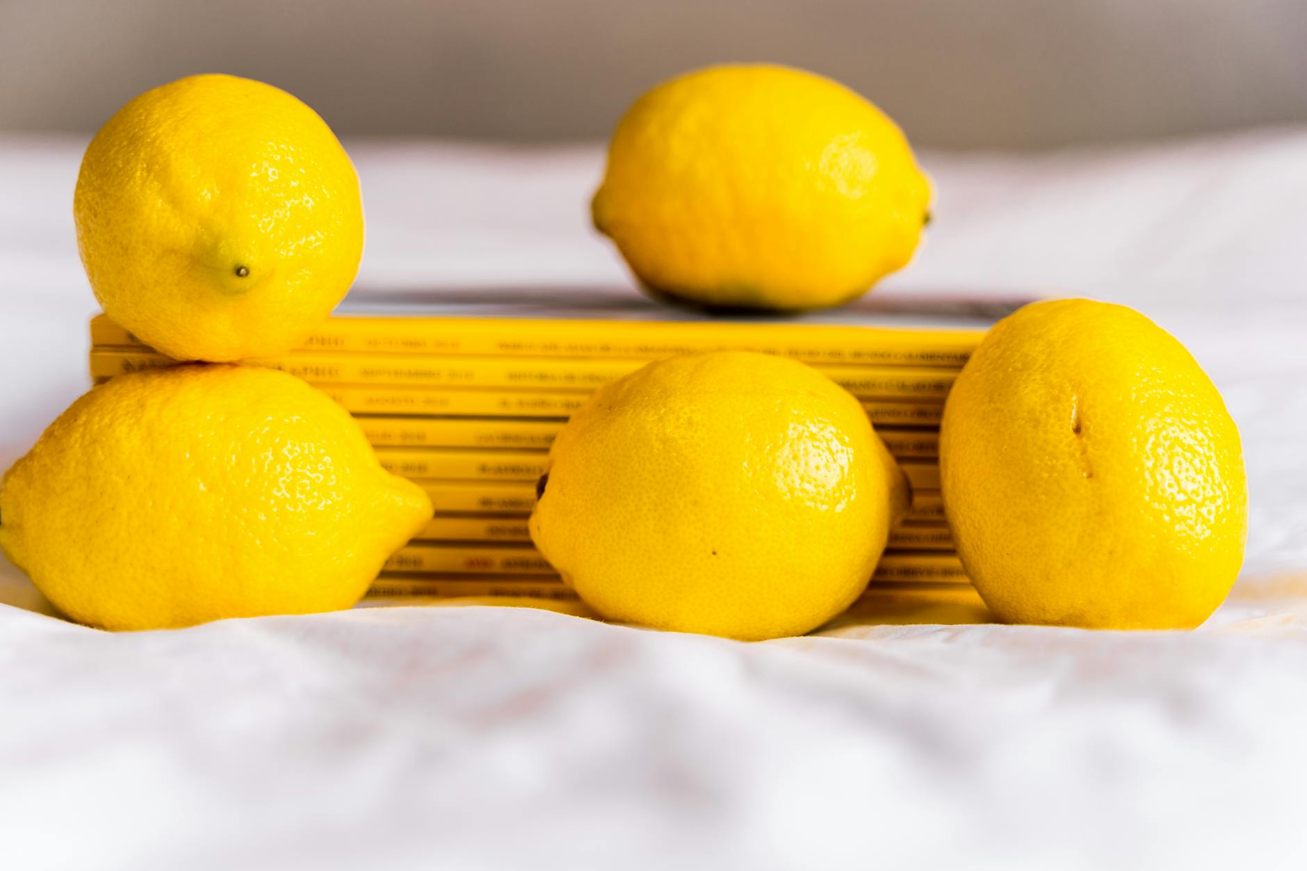 Hand holding fresh lemon on soft pink background with additional lemons
